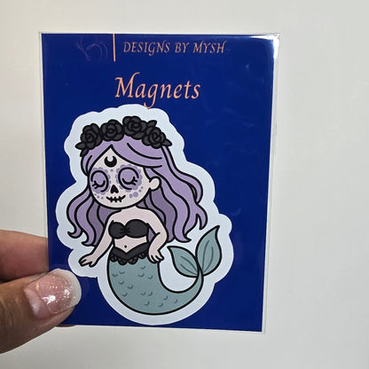 Sticker with artistic design on a blue card held by a hand, with a grid-patterned wall in the background.