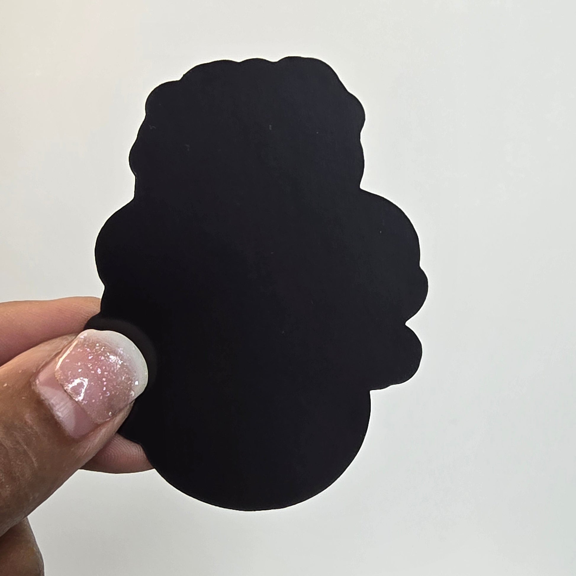 Black cloud-shaped object held by a hand with glittery nail polish against a white background.