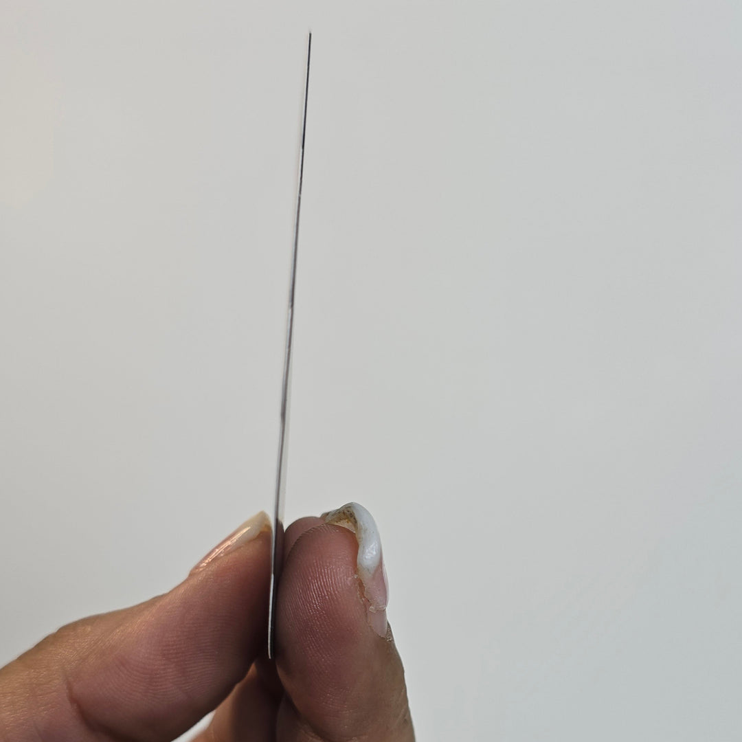 Hand holding a thin black object against a light gray background
