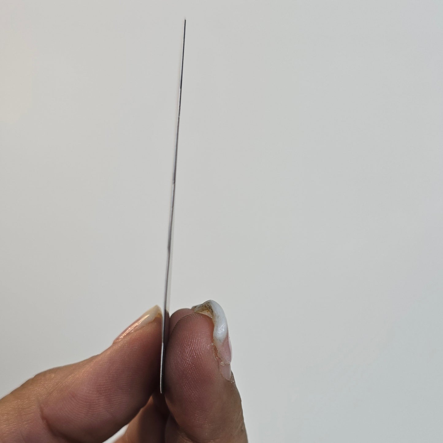 Hand holding a thin black object against a light gray background