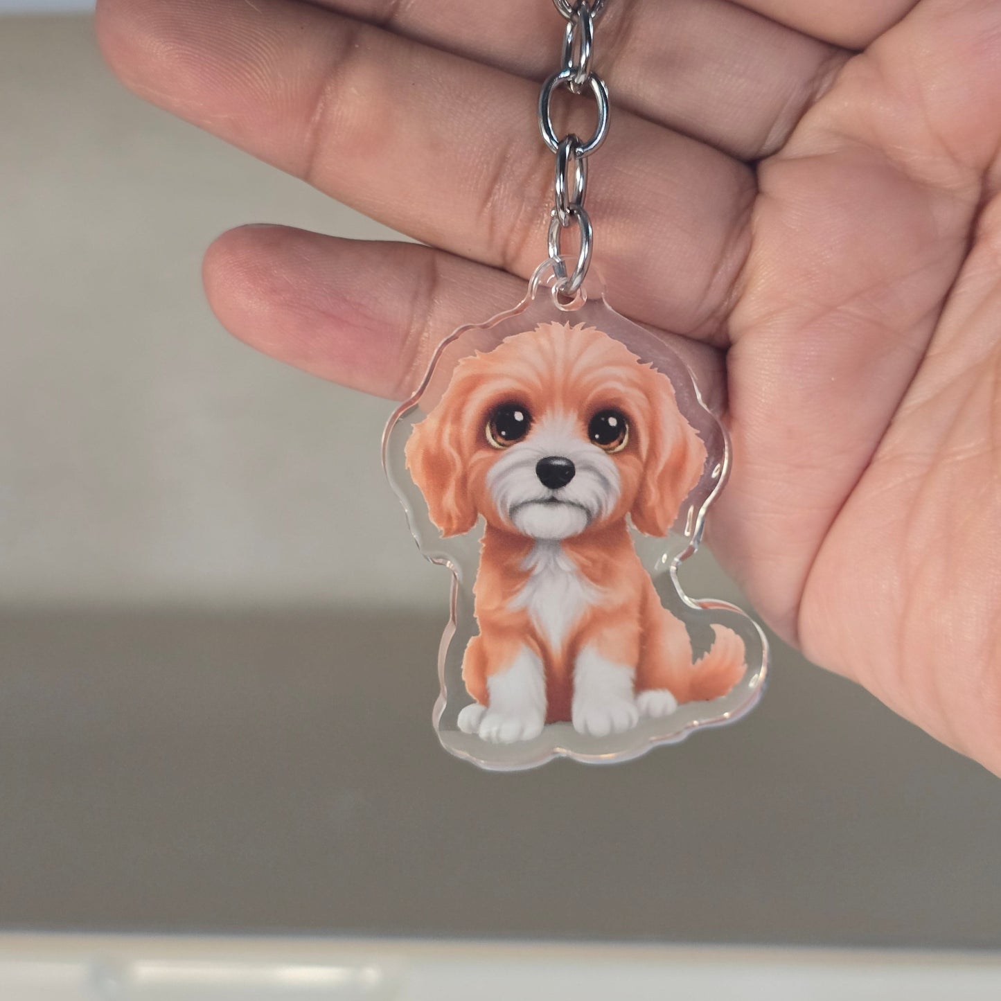 Hand holding a keychain with a dog design against a neutral background