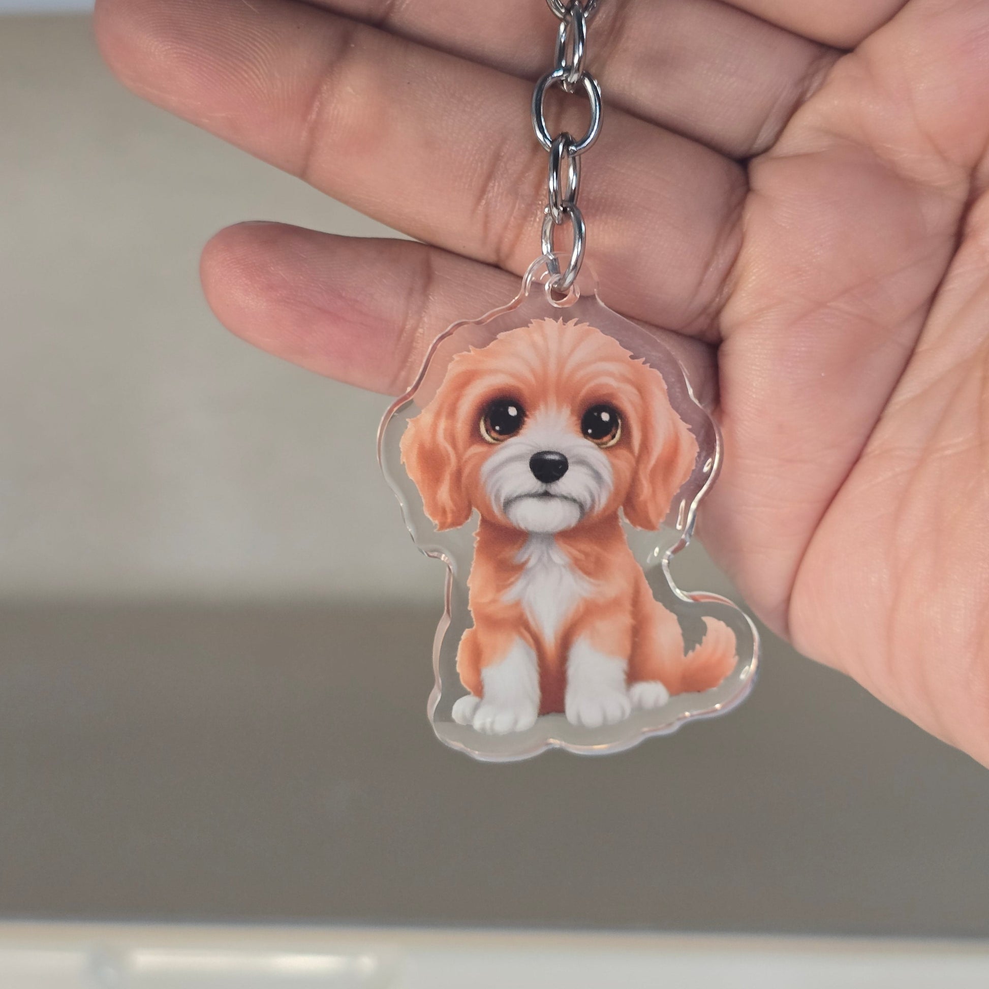 Hand holding a keychain with a dog design against a neutral background
