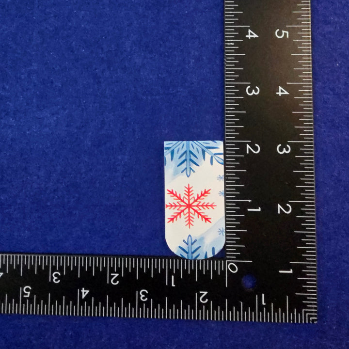 Small rectangular fabric sample with snowflake pattern on a blue background, measured against a ruler.