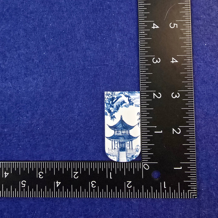 Small blue and white ceramic tile with architectural design on a blue background with ruler for scale.