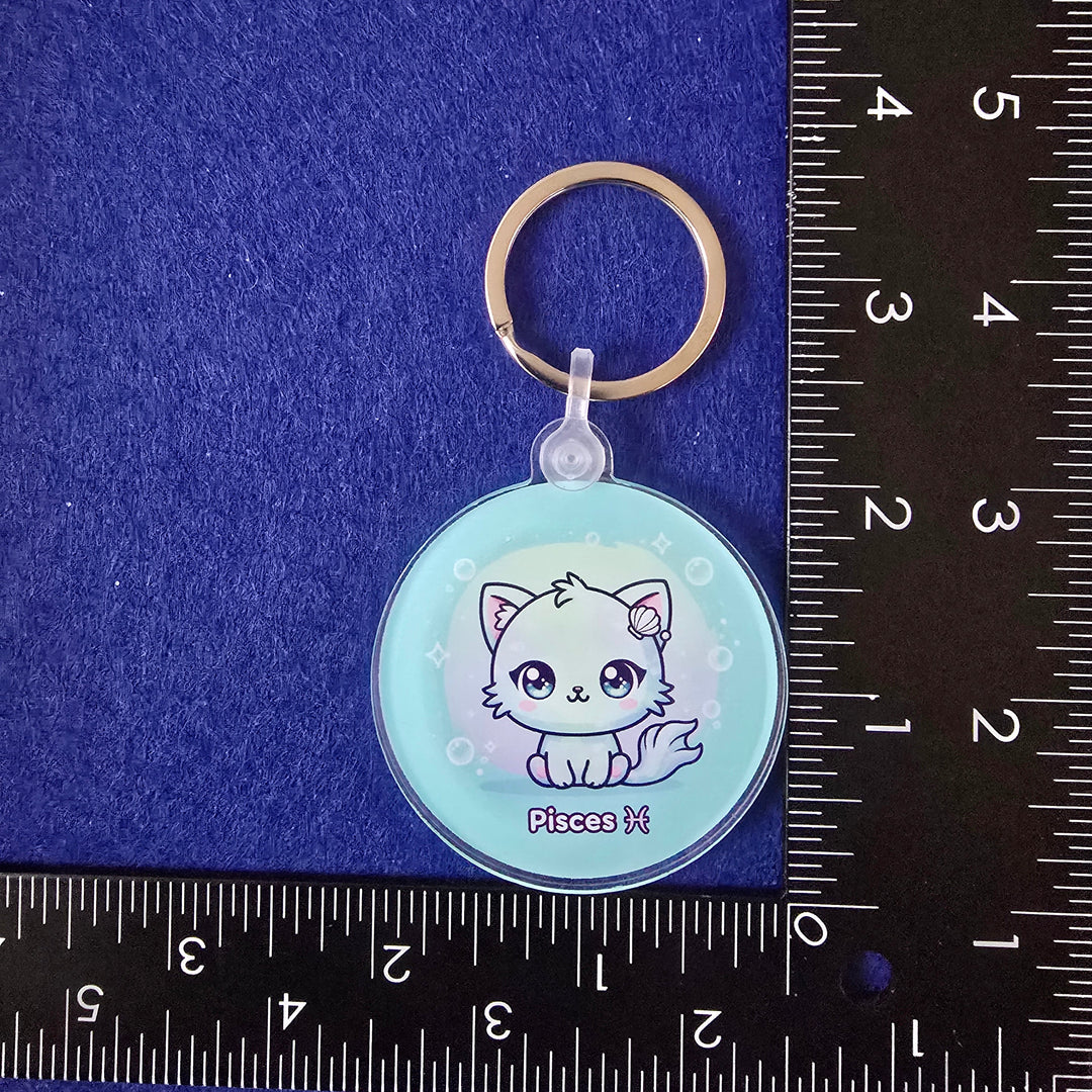 Keychain with a cat design on a blue surface with a ruler for scale.