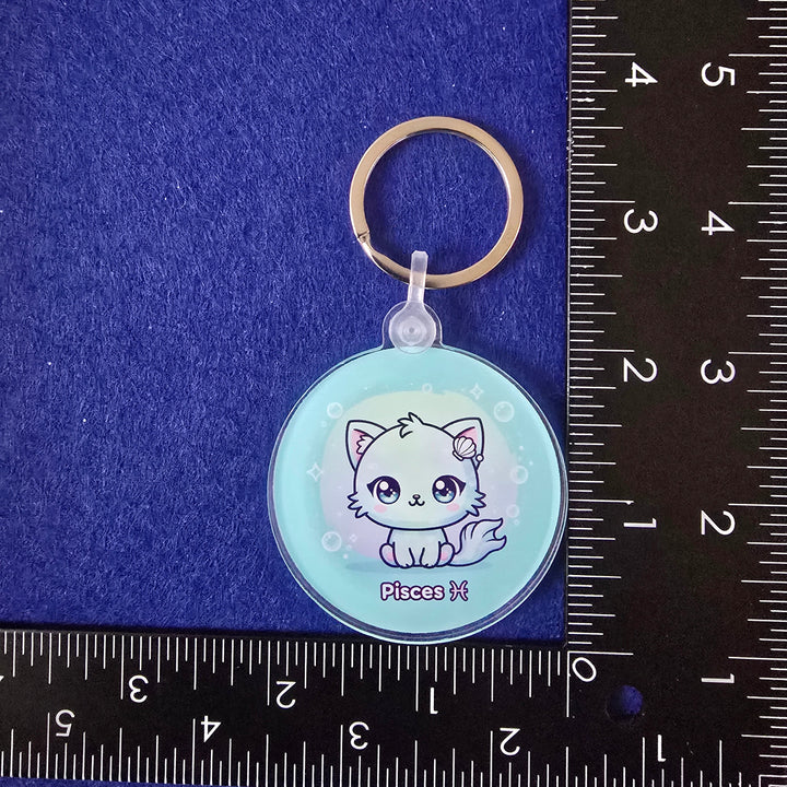 Keychain with a cat design on a blue surface with a ruler for scale.
