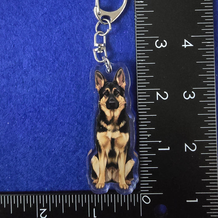 Dog-shaped keychain with clear plastic backing on a blue surface with a ruler for scale.
