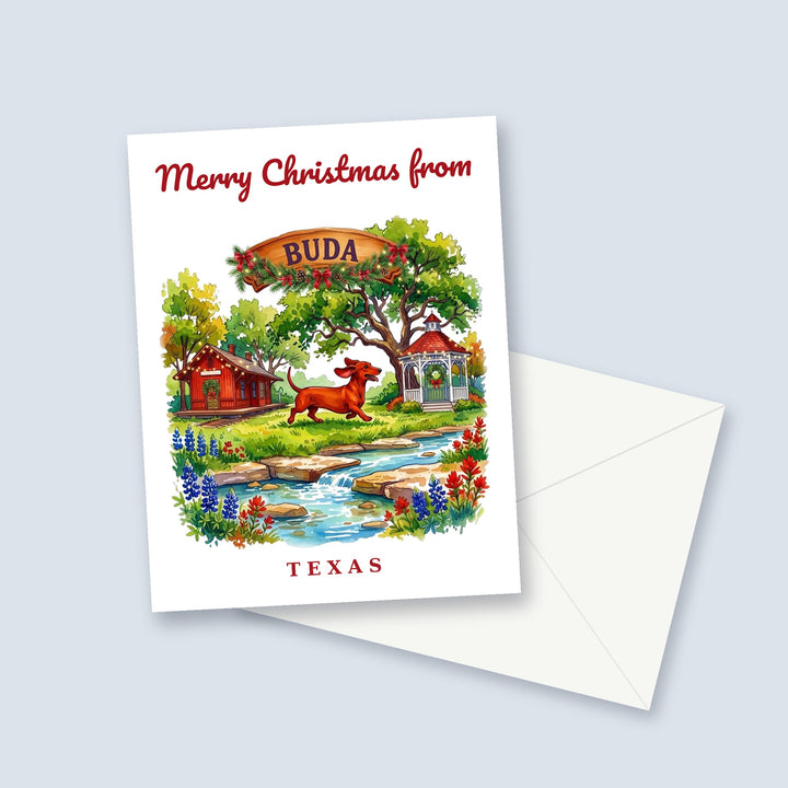 Merry Christmas from Buda Texas watercolor Christmas card with a wiener dog, the depot and bluebonnets, a garland-trimmed town sign and a white envelope