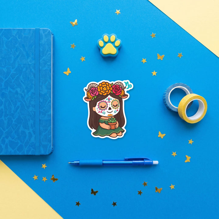Capricorn sugar skull girl 3 inch sticker flat lay with blue and yellow stationery – Designs by Mysh