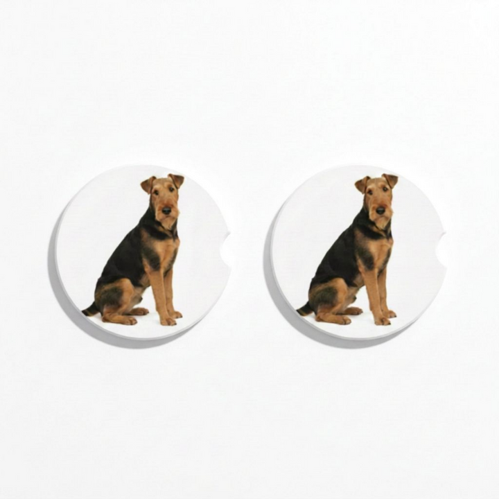 Set of two round ceramic car coasters featuring a watercolor-style illustration of an Airedale Terrier with a black and tan coat.