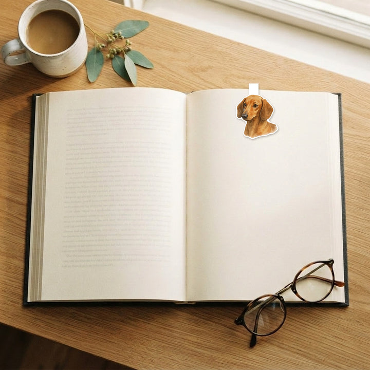 Dachshund magnetic bookmark on an open book on a wooden desk with coffee and reading glasses