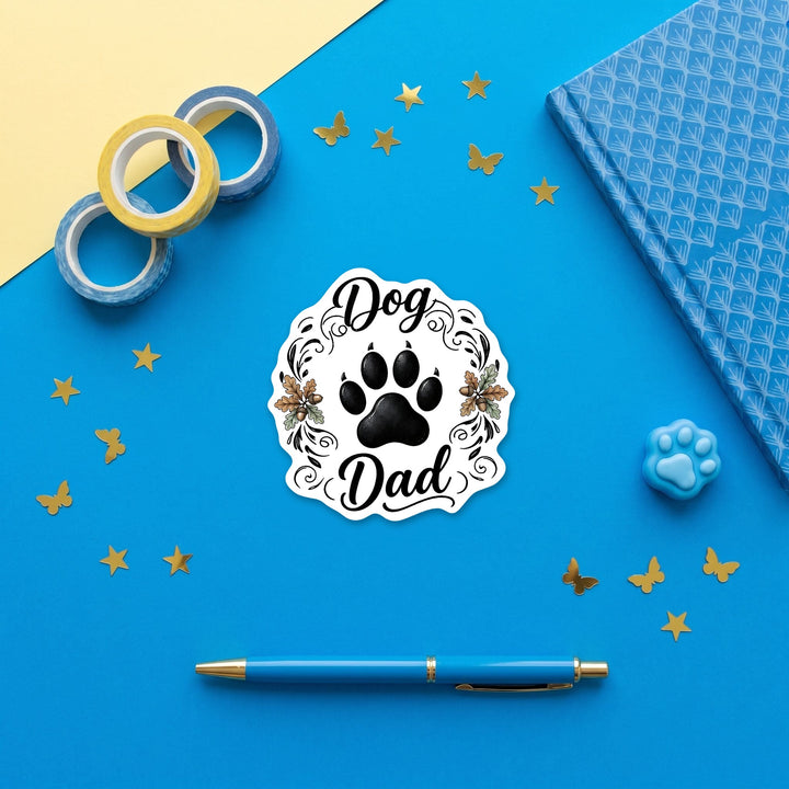 Dog Dad paw print sticker in a blue flat lay with washi tape, a notebook and a pen