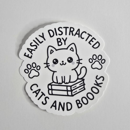 "Die-cut vinyl sticker with a black-and-white kawaii cat sitting on books, surrounded by the text 'Easily Distracted by Cats and Boooks' and two paw prints."