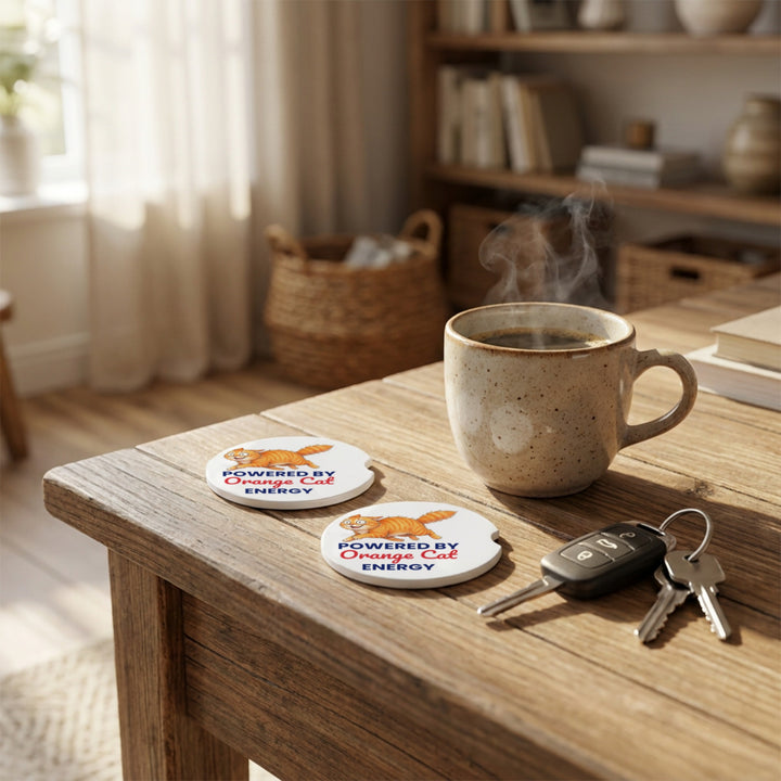 Two Powered By Orange Cat Energy car coasters on a wooden table with a mug and car keys