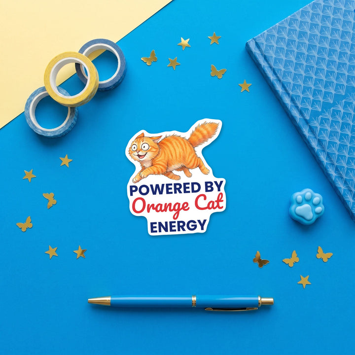 Powered By Orange Cat Energy orange cat sticker in a blue flat lay with washi tape and a pen