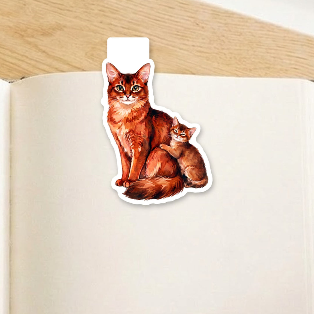 Somali cat mama and kitten watercolor magnetic bookmark clipped over the top of an open book page – Designs by Mysh