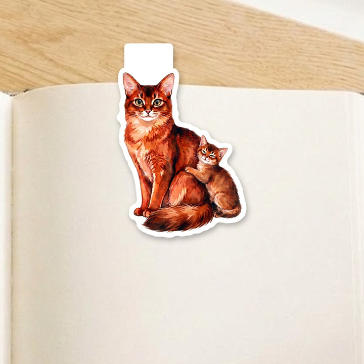 Somali cat mama and kitten watercolor magnetic bookmark clipped over the top of an open book page – Designs by Mysh