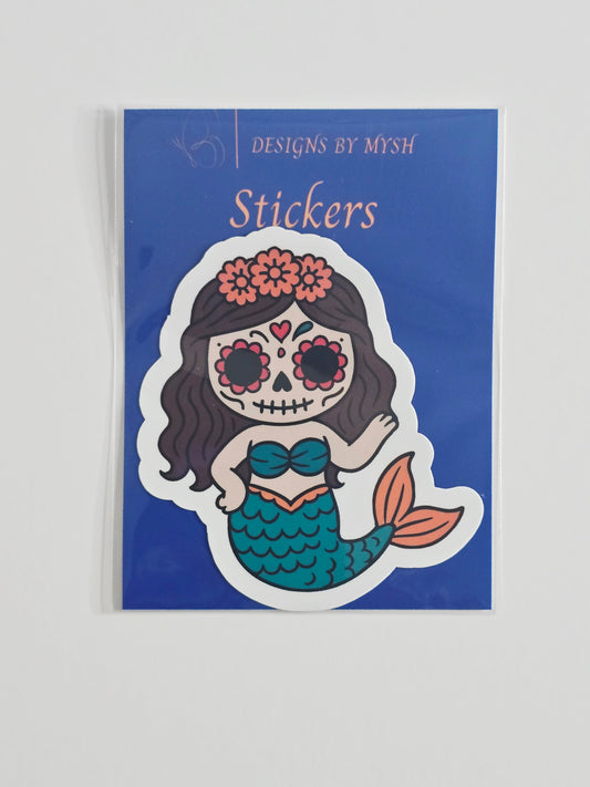 "Cartoon sugar skull mermaid with long dark hair, floral crown, and turquoise tail, printed on a 3-inch water-resistant vinyl sticker with glossy laminate finish."