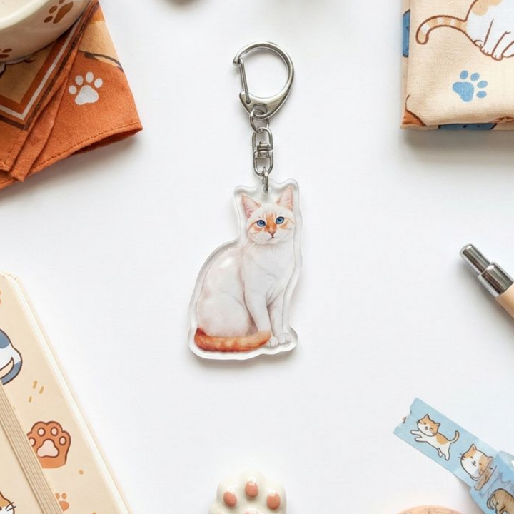 Flame point Siamese cat acrylic keychain in a styled flat-lay with matching cat-themed stationery and accessories