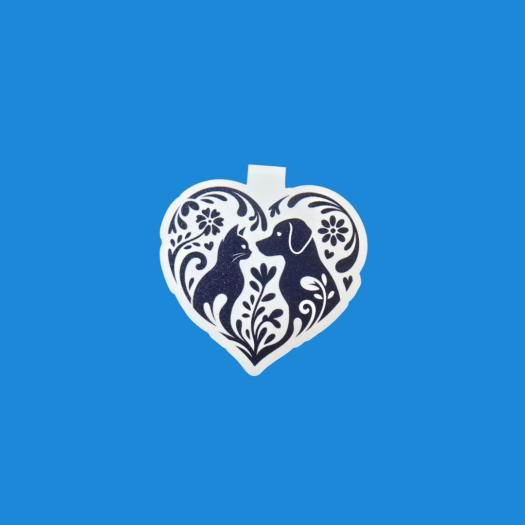 A white heart-shaped ornament featuring a navy blue silhouette of a dog surrounded by floral patterns, shown against a solid blue background.