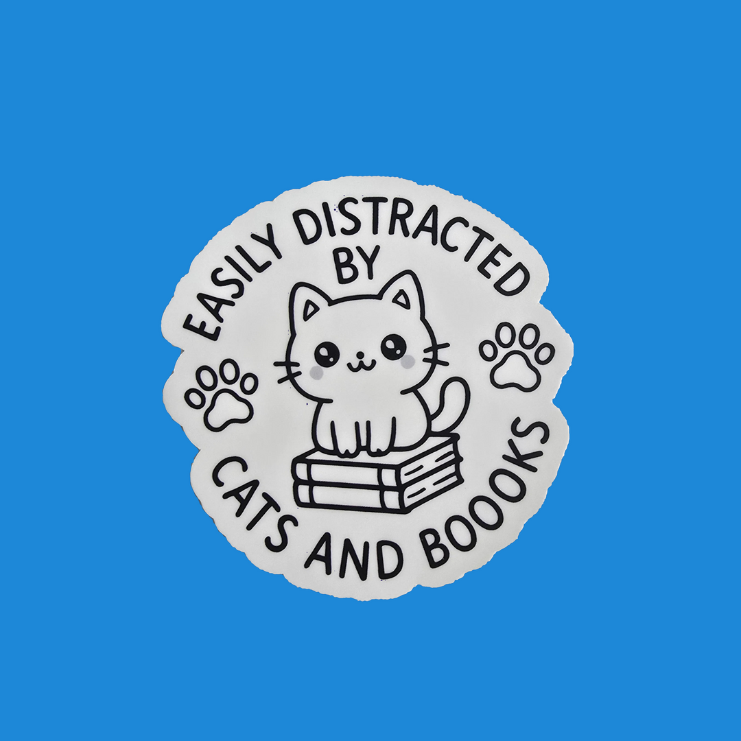 A die-cut sticker featuring a cute black line art illustration of a cat sitting on books, surrounded by the text 'EASILY DISTRACTED BY CATS AND BOOKS' and paw prints, shown on a solid blue background.