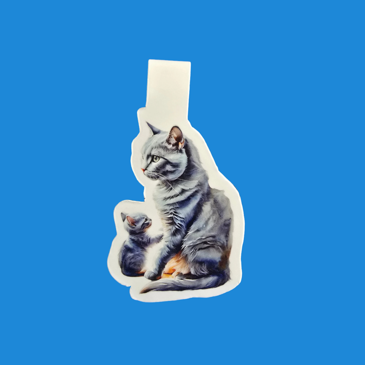 A die-cut sticker featuring a realistic illustration of a gray tabby cat and a small kitten, shown on a solid blue background.