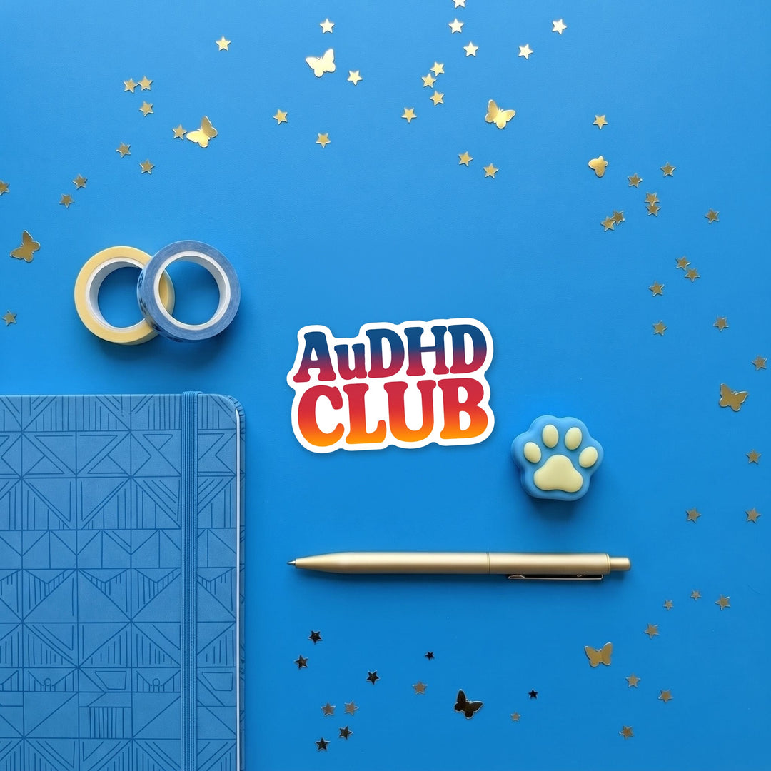AuDHD CLUB sticker in a brand flat lay with a notebook and pen