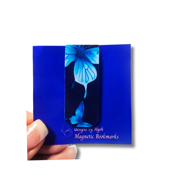 Blue magnetic bookmarks with butterfly design held by a hand on a white background