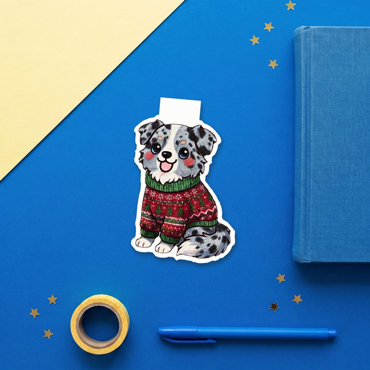 Blue merle Australian Shepherd in ugly Christmas sweater kawaii magnetic bookmark flat lay with blue stationery – Designs by Mysh