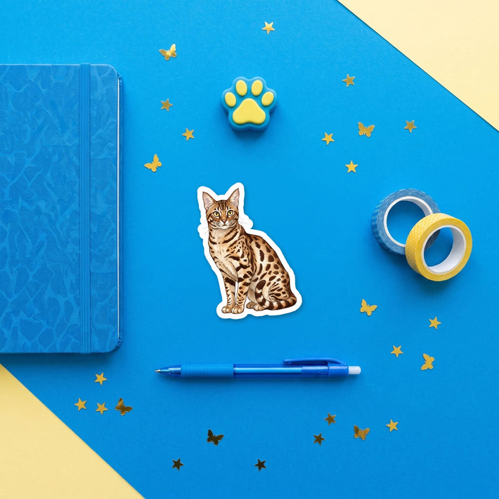 Ocicat Chocolate Spotted watercolor 3 inch sticker flat lay with blue and yellow stationery – Designs by Mysh